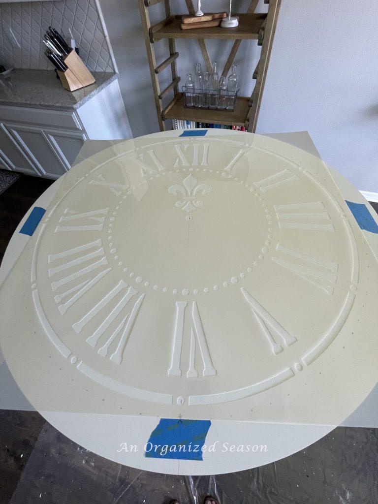 Step six to makeover a table set with paint and a stencil is to tape the stencil in place.