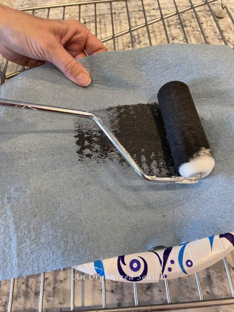 Step eight to makeover a table set with paint and a stencil is to offload the paint roller on a paper towel.