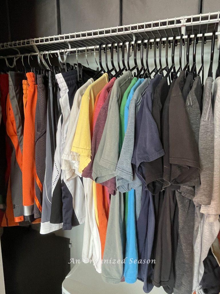 T-shirts and shorts hanging in a closet, showing how to teach your kid how to organize a closet.