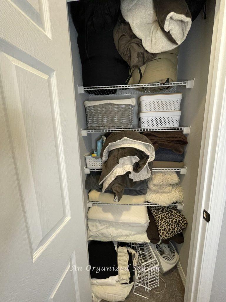 A closet overstuffed with linens that needs advice for organizing a linen closet.