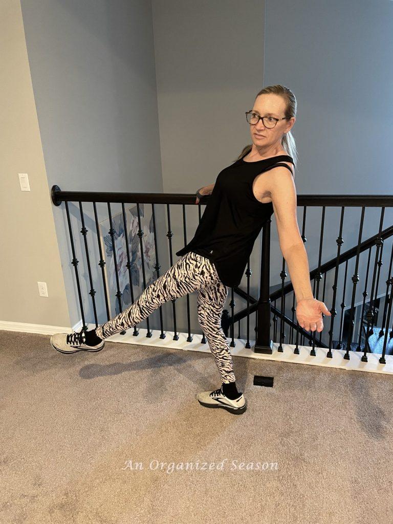 A woman in exercise clothes holding a railing like a ballet barre, exercising as part of her morning routine.