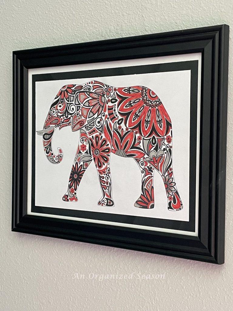 An elephant colored red, black, and gray in a black frame. Part of a   boring bedroom makeover for a gamer.