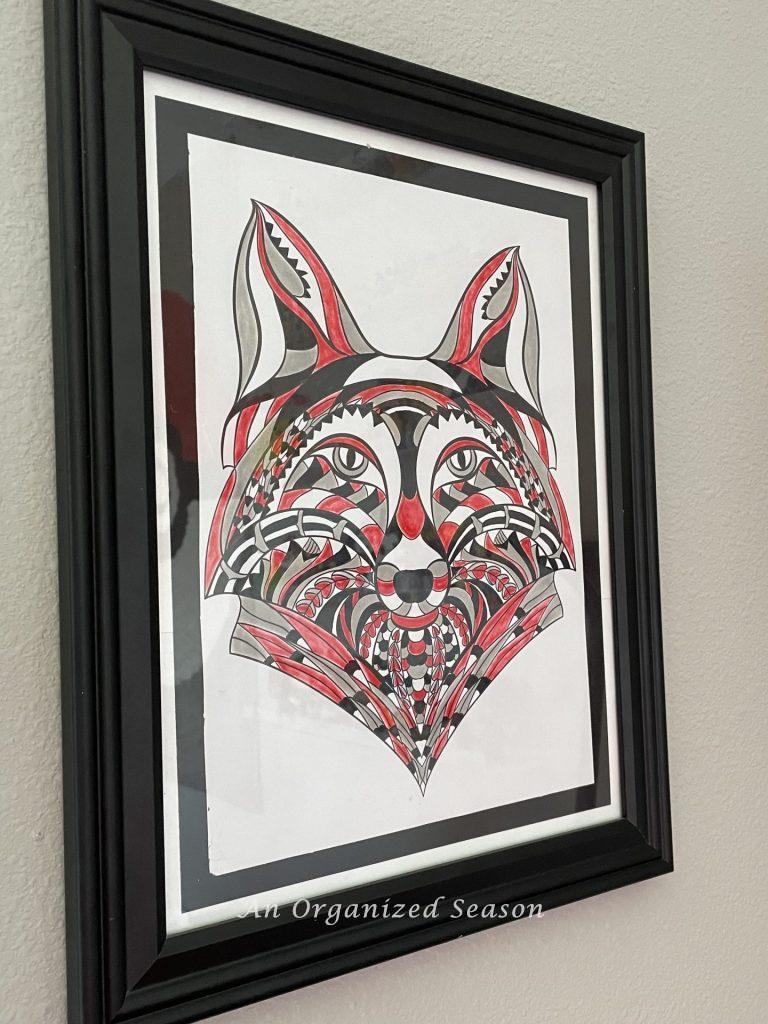 A wolf face colored red, black, and gray in a black frame is part of   boring bedroom makeover for a gamer.