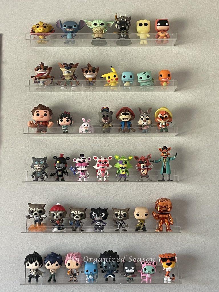 Six clear shelves hanging on a wall displaying POP figures. 
