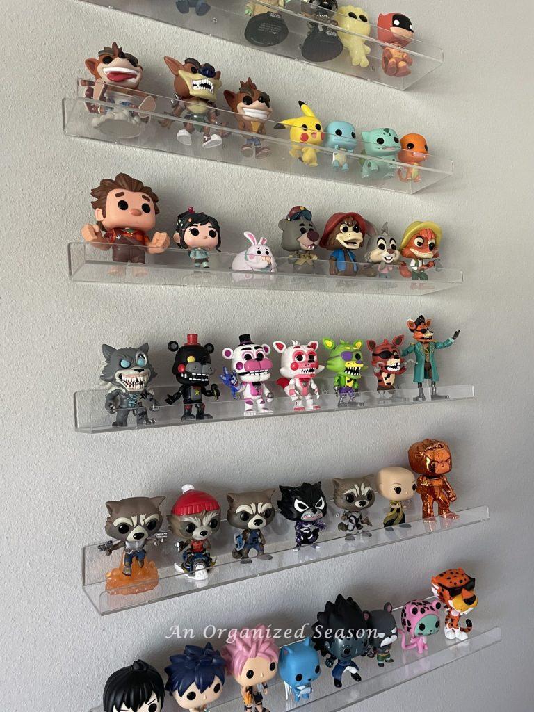 Clear shelves hanging on a wall that contain POP figures showing tips to organize collections in a kid's bedroom! 