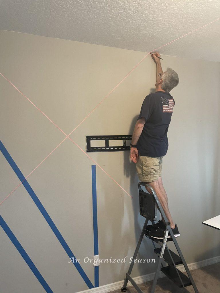 Man using a laser level to mark lines on a wall to build a modern accent wall in a bedroom.