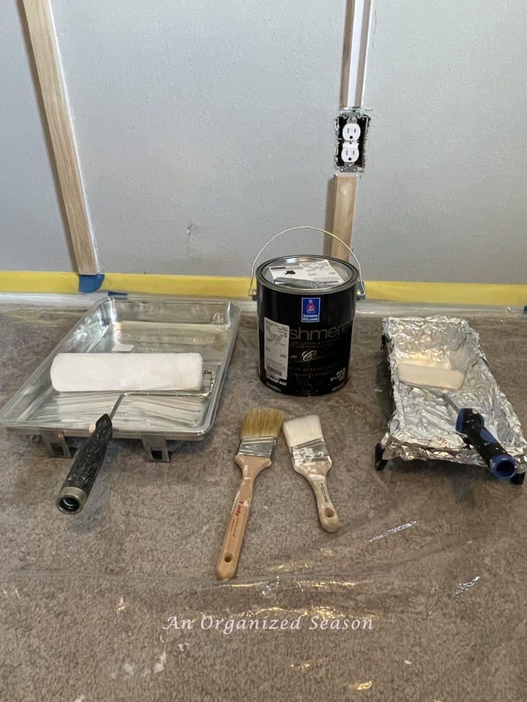 Paint, rollers, brushes, and pans used to paint a modern accent wall in a bedroom.