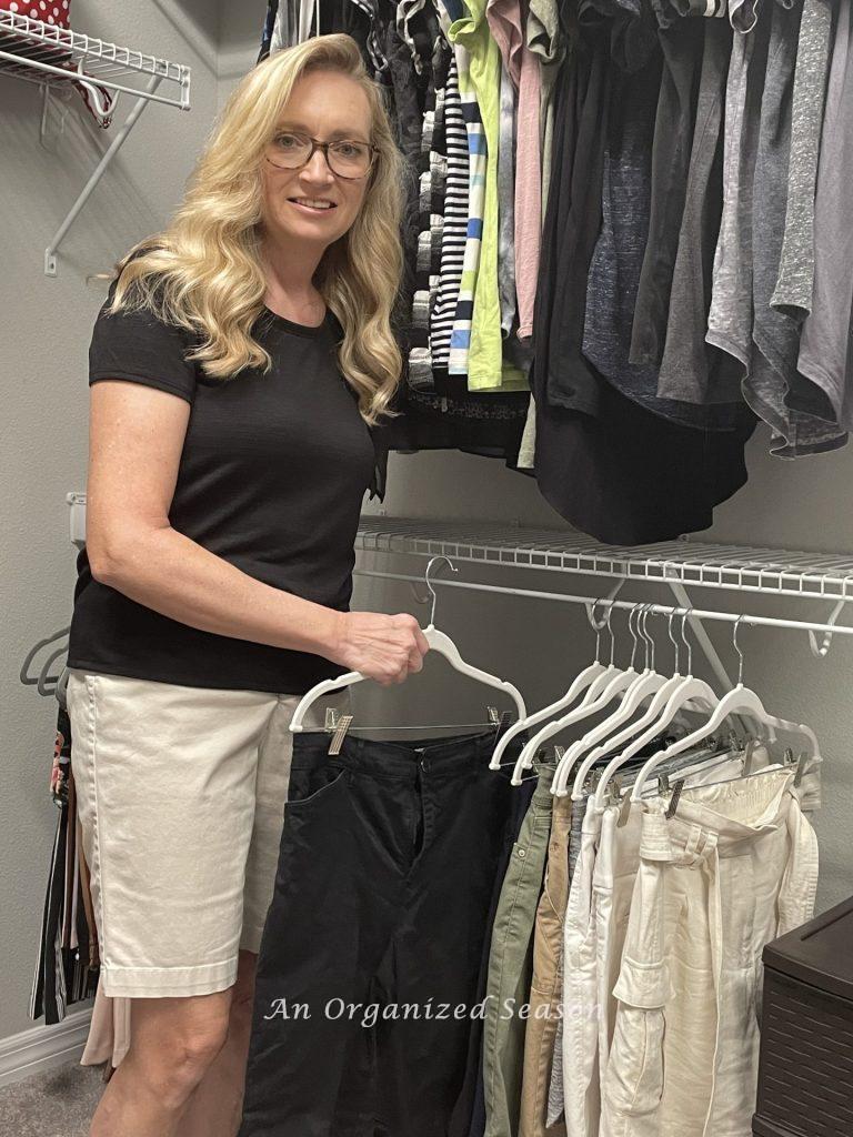 A woman hanging a pair of shorts in an organized closet. 