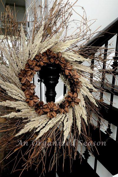 Twig wreath decorated with off white evergreen stems and a circle of pinecone flowers.