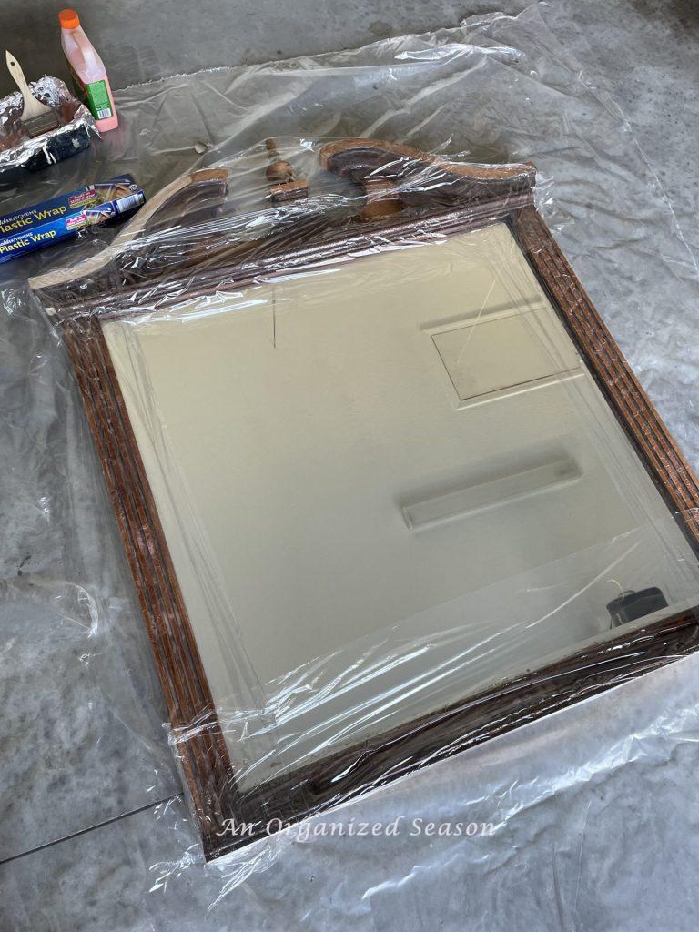 A mirror covered in Citristrip and plastic wrap showing how to strip and bleach wood furniture. 