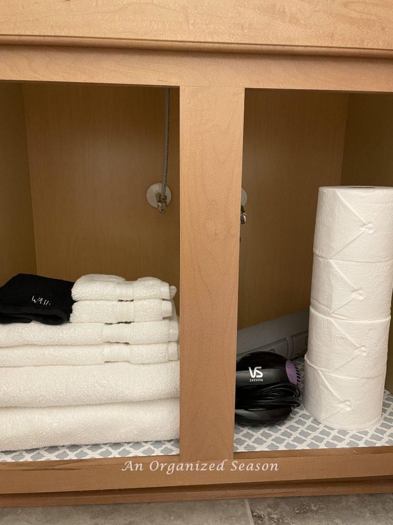 Organize the guest bath cabinet with towels, toilet paper, and a blow dryer.