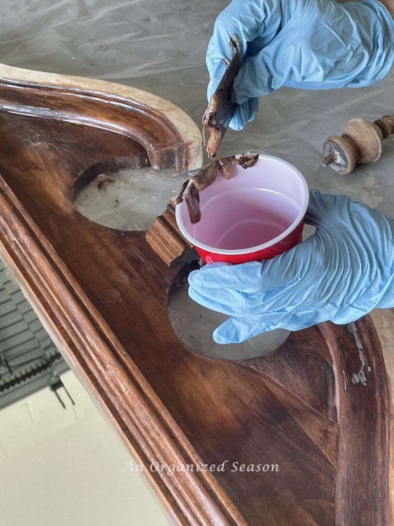 Someone removing Citristrip from a mirror showing how to strip and bleach wood furniture. 