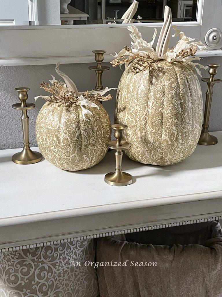 Two gold and white decoupage pumpkins sitting on an entryway table. 