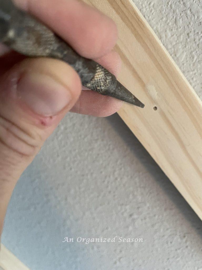 A man setting a nail in a board, step three to build a modern accent wall in a bedroom.