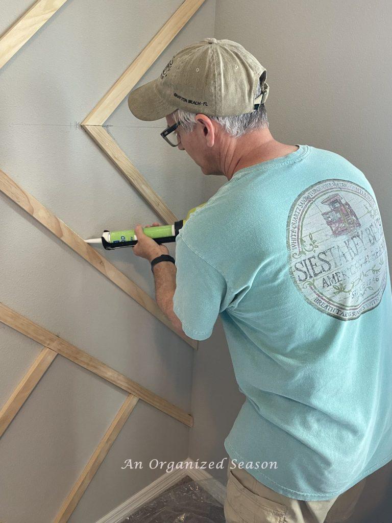 A man caulking 2 inch boards, step six to build a modern accent wall in a bedroom.