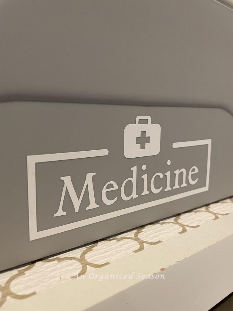 Gray container with a white label that says "medicine." An example of how to store medicine when organizing your home. 
