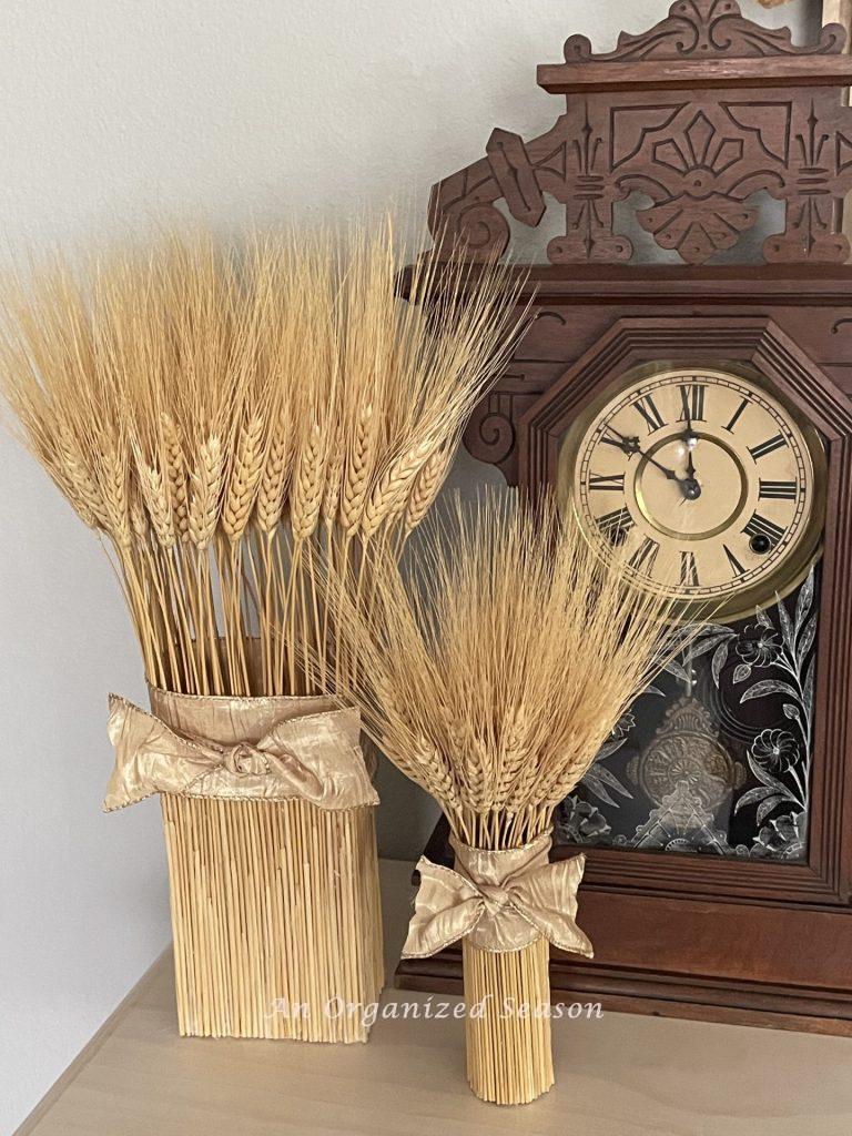 Two dried wheat arrangement bundles sitting in front of an antique clock.