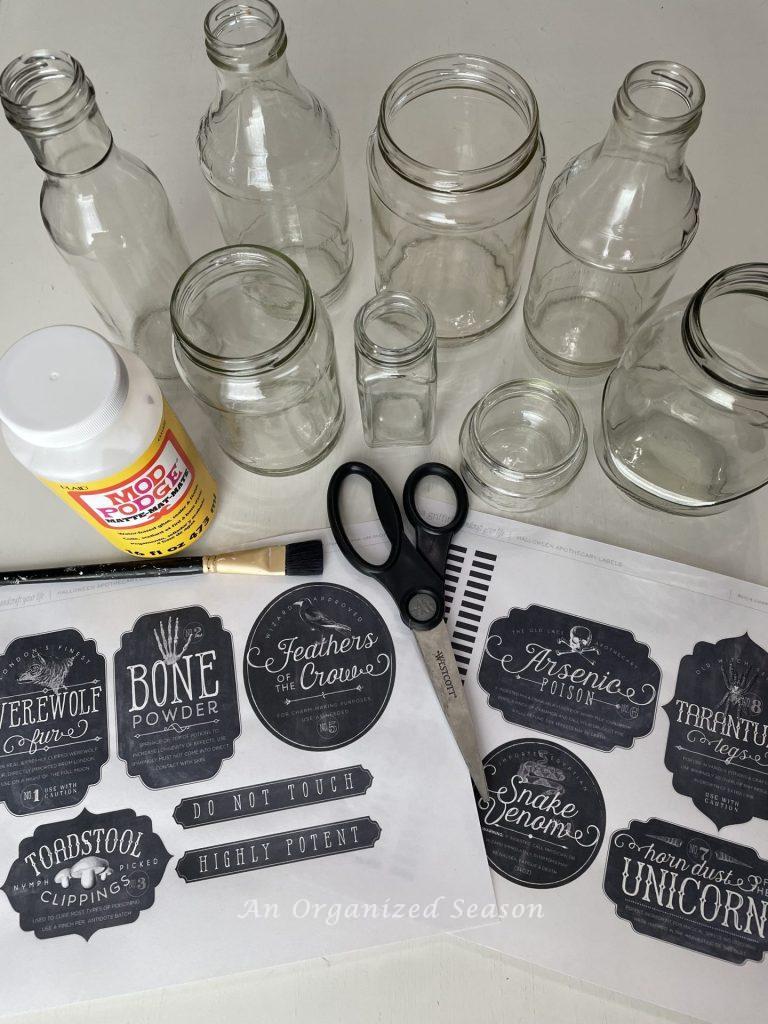 Glass jars, labels, scissors, Mod Podge, and a paintbrush, items needed to make spooky potion bottles from jars!