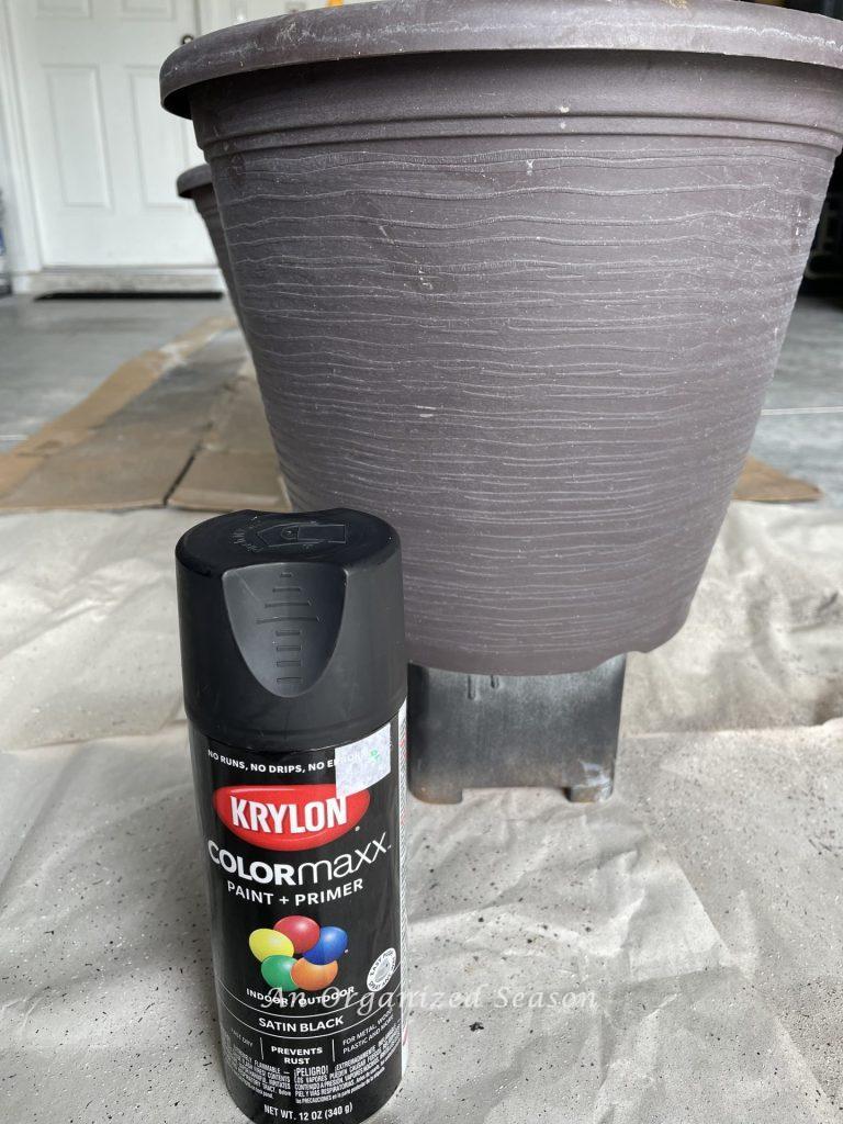 Two brown flower pots with a can of black spray paint, that will hold the pumpkin obelisks. 