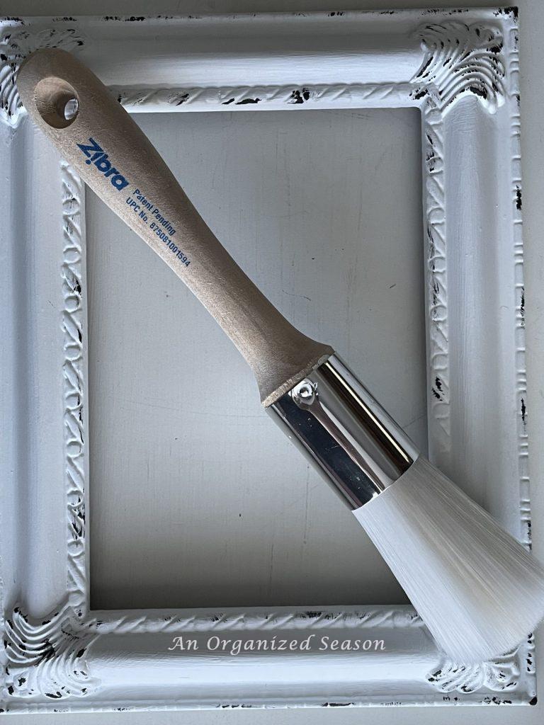 A round Zibra paint brush sitting on a white picture frame. 