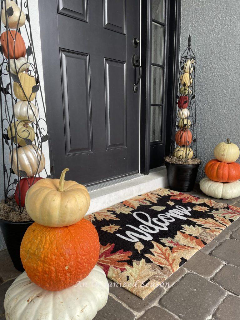 Two pumpkin obelisks on either side of a door. A stack of three pumpkins sits in front of each one. 