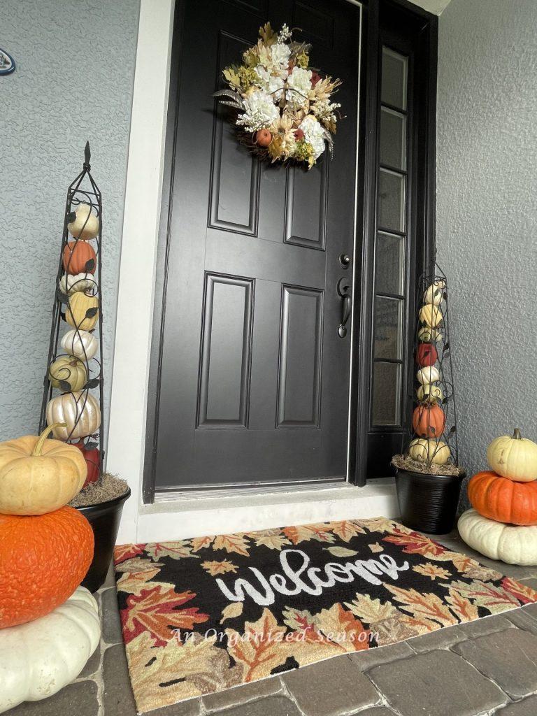 A front door flanked by two pumpkin obelisks and two stacks of pumpkins.