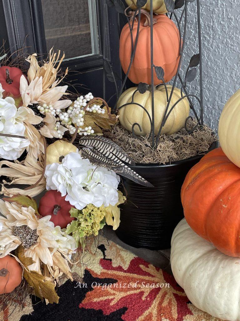 A rug, pumpkins, and a wreath used to decorate a front porch.