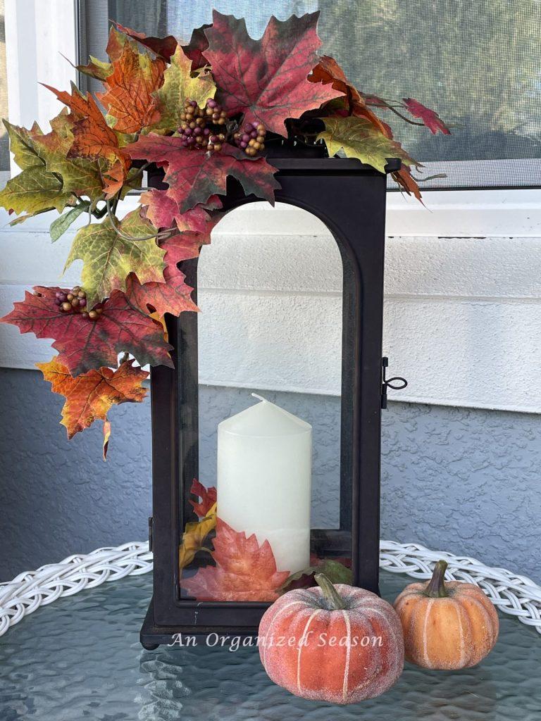 A brown metal lantern with a candle, decorated with fall leaves. Reuse this old lantern for a Budget decorating ideas for fall porch.