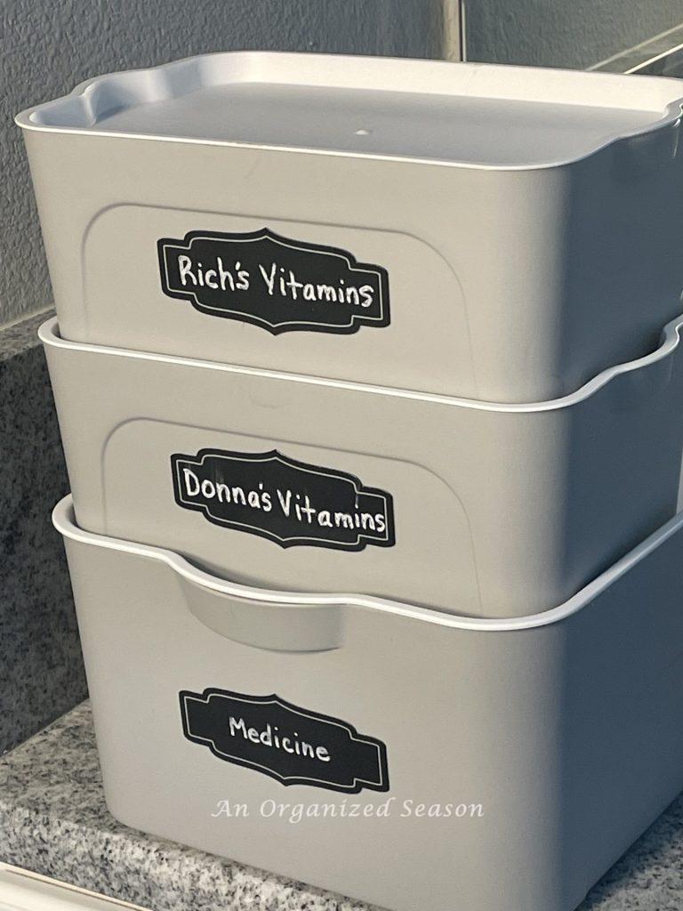 Three stacked gray plastic tubs with black labels showing how to organize medicine in your home. 