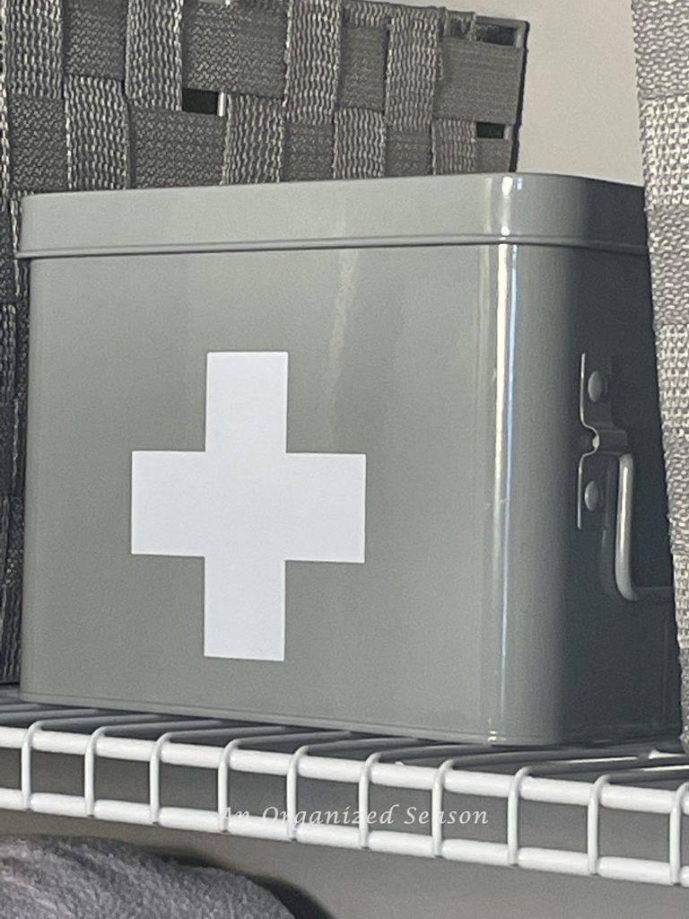 A gray metal container with a white cross on it, used to organize medicine in your home.