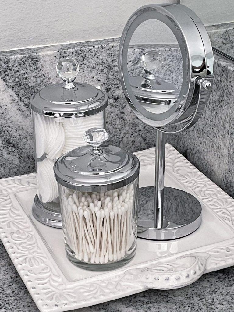 Clear canisters and a mirror on a tray on bathroom counter.