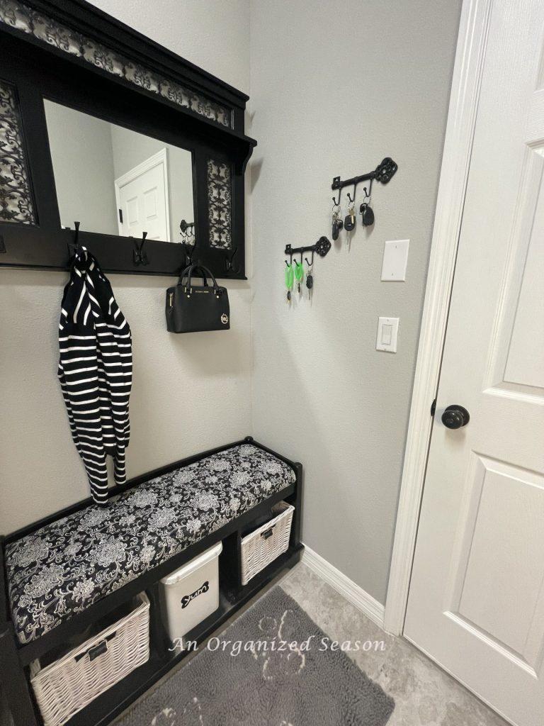 A storage bench and a matching mirror with hooks holding a purse and jacket.  