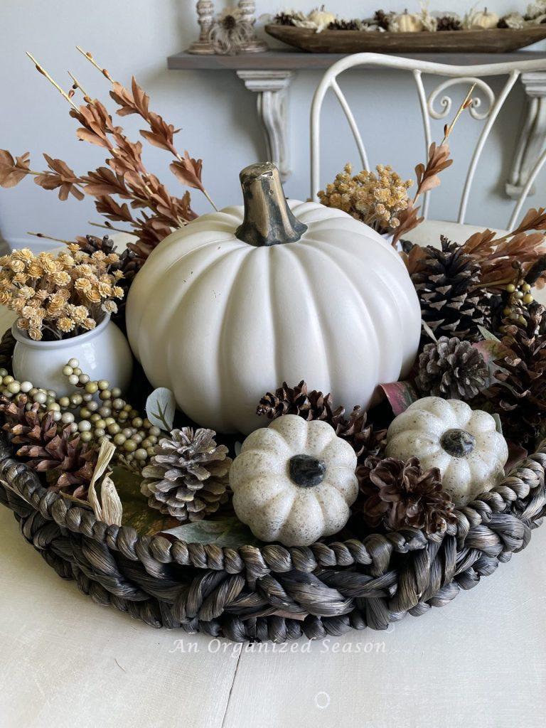 A round basket holding white pumpkins and pinecones. 