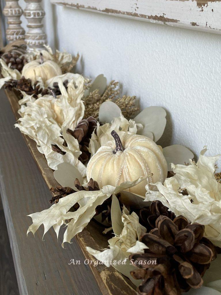 A dough bowl filled with white velvet pumpkins, dried leaves, and pinecones. 