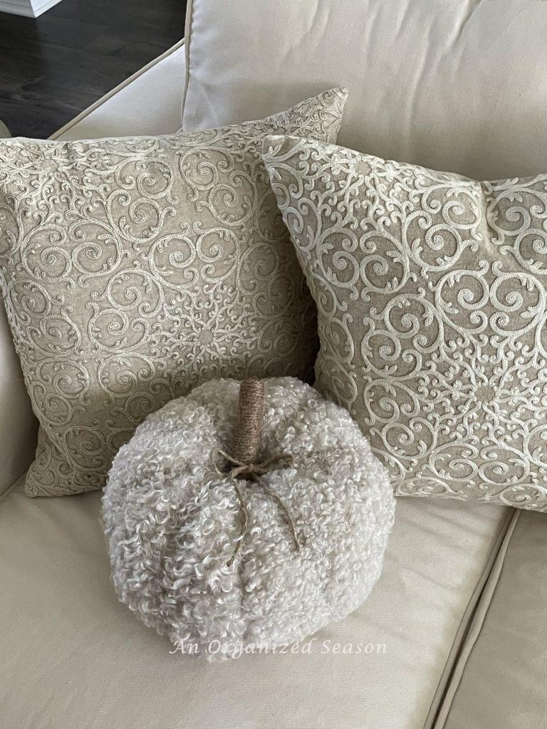 A pillow shaped like a pumpkin sitting in front of two decorative pillows on a couch. 