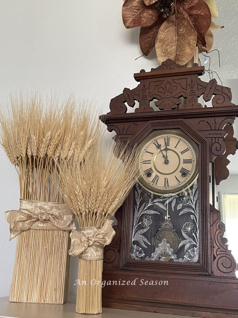 An antique clock and two dried wheat bundles. 