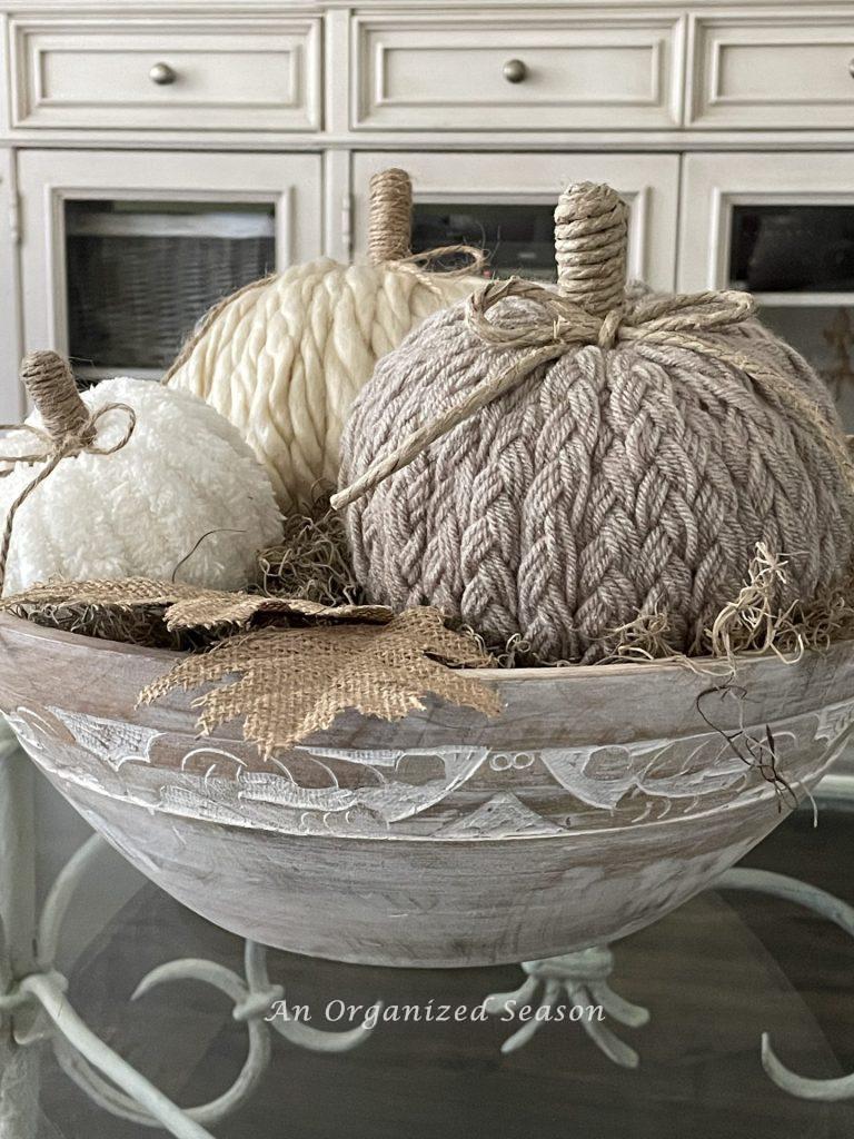 Three yarn pumpkins inside a wooden bowl. 