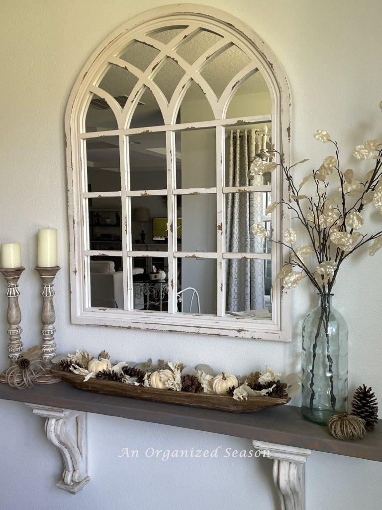 A shelf with a mirror above it, decorated for Fall. 