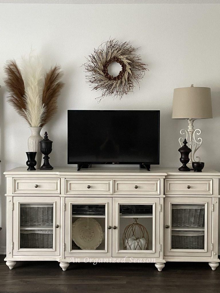 A TV console table with glass doors that's decorated for Fall. 