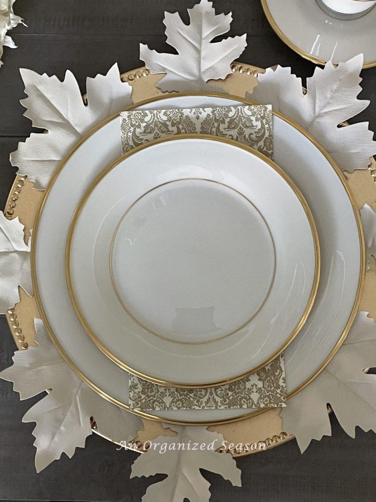 Cream colored china on a gold charger with white leaves. 