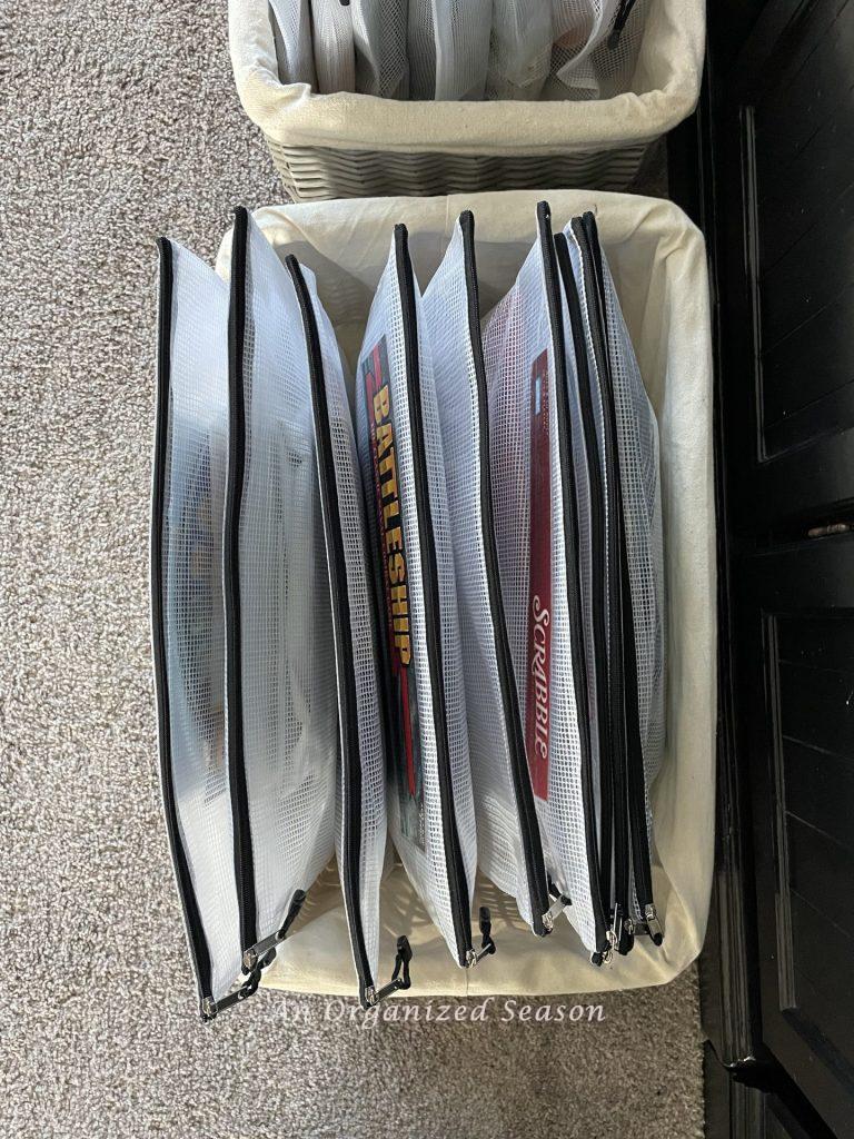 Board games organized in zipper bags and stored in a large basket. 