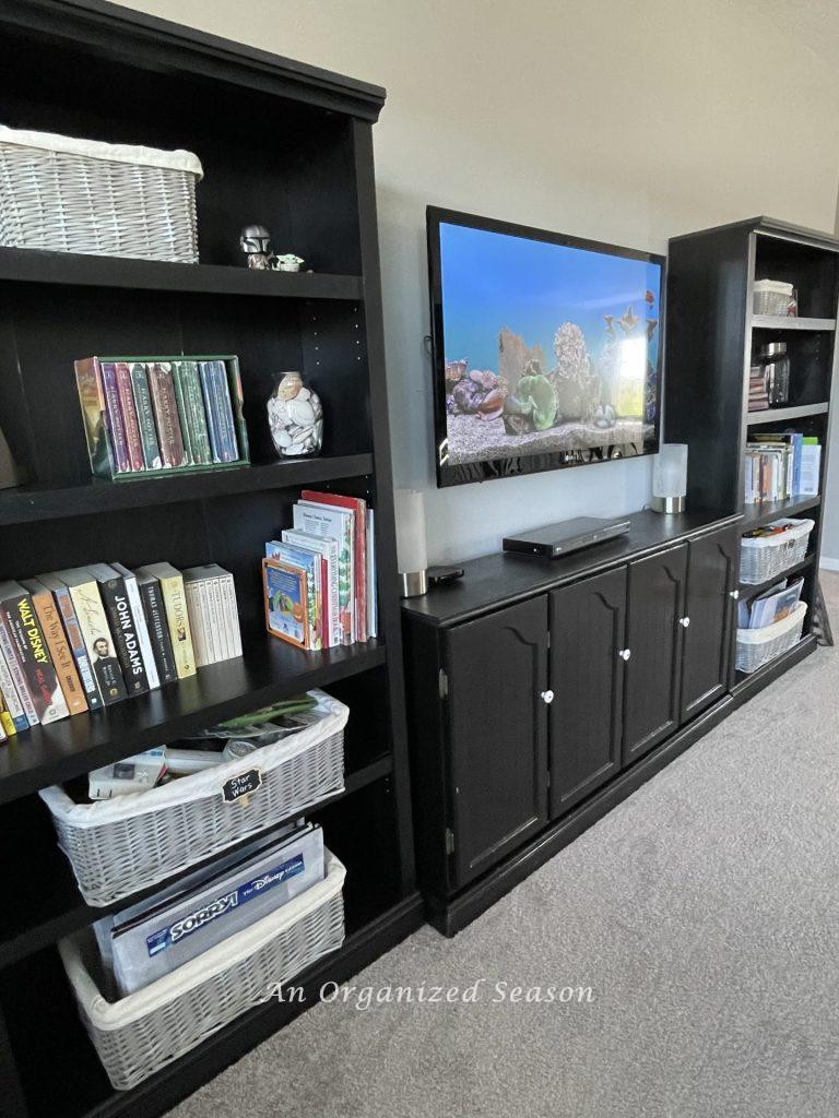 Two organized black bookshelves and a black cabinet in between them.