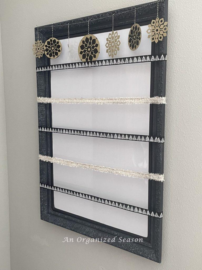 A hanging whiteboard with five pieces of ribbon and a garland going across it.