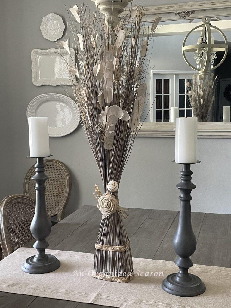 Gray candlesticks and a dried flower arrangement on a dining room table. 