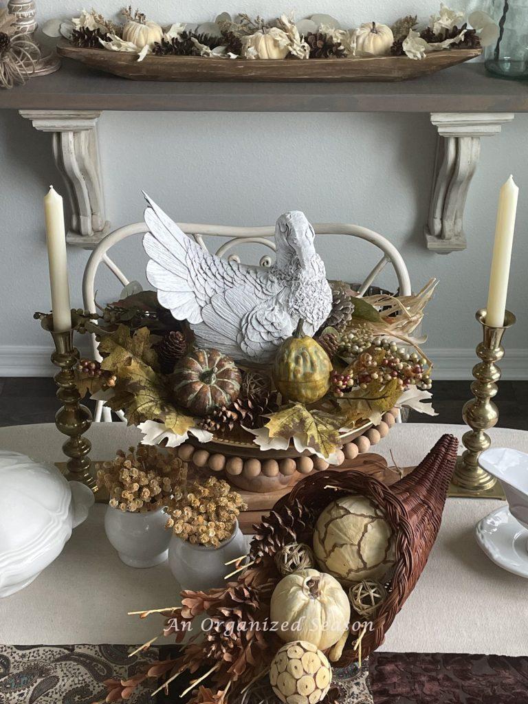 Thanksgiving centerpiece using a white turkey on a cake stand and a cornucopia filled with orbs. 