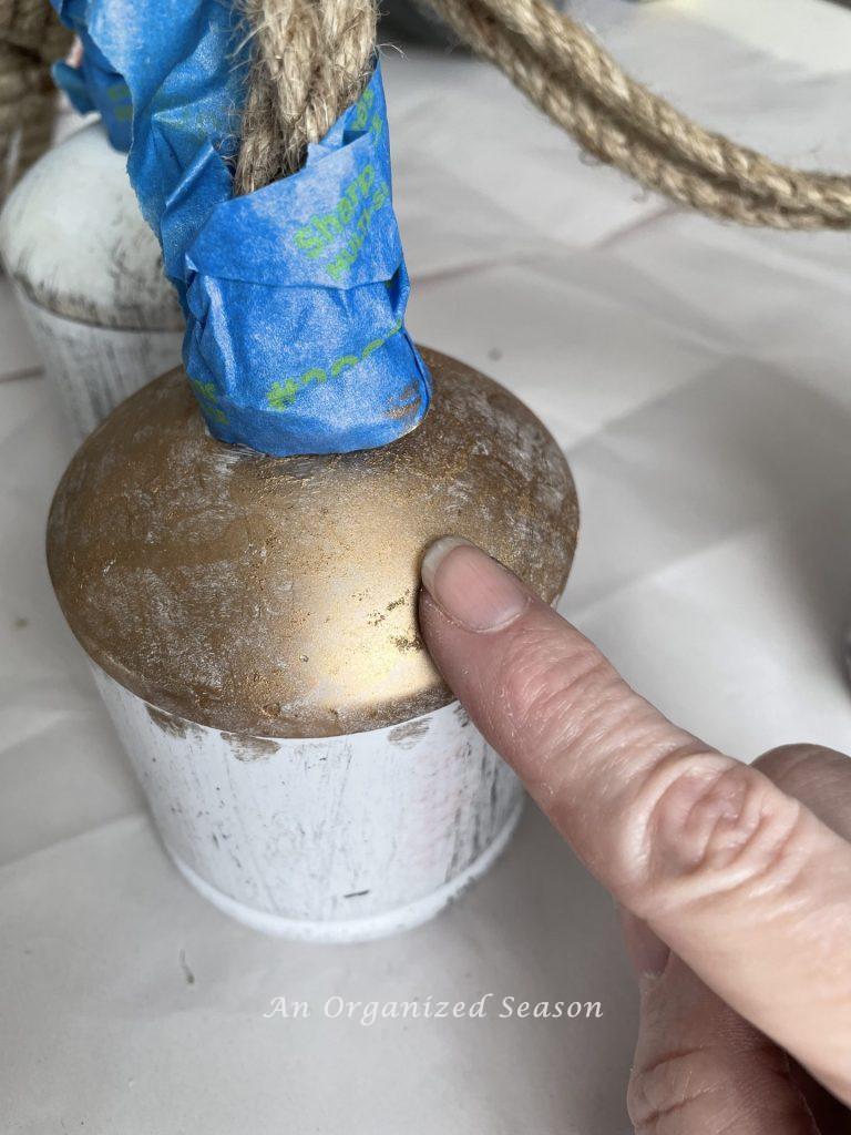 A finger applying gold to a bell creating a Pottery Barn rustic iron bell hack.