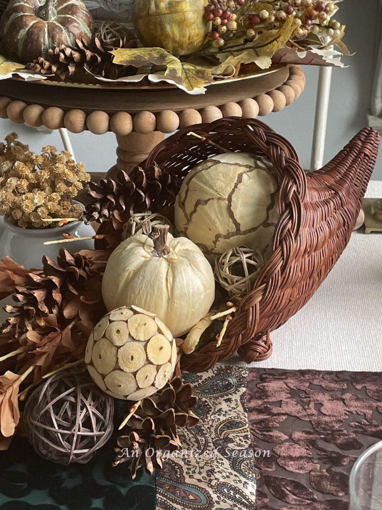 A cornucopia filled with decorative neutral orbs and pinecones. 