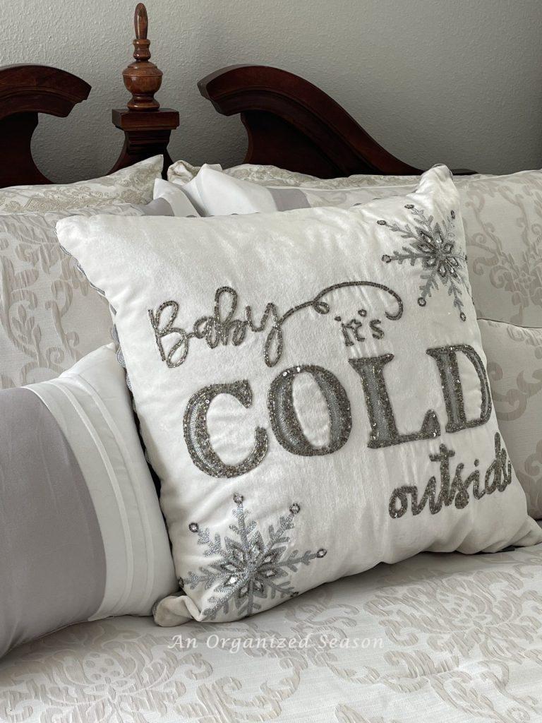 Pillows on a bed, one is embroidered with the words "baby it's cold outside." 