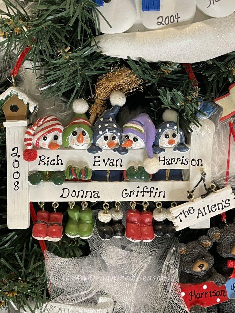 A personalized Christmas ornament showing five snowmen wearing hats and standing behind a fence, an example of our family keepsake ornament tradition.