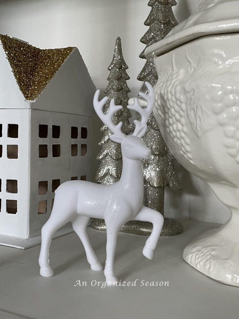 White deer styled next to a house in a Christmas village. 